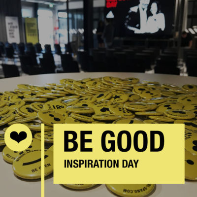 Bright yellow buttons with positive messages promote “Be Good Inspiration Day” at a lively event space.