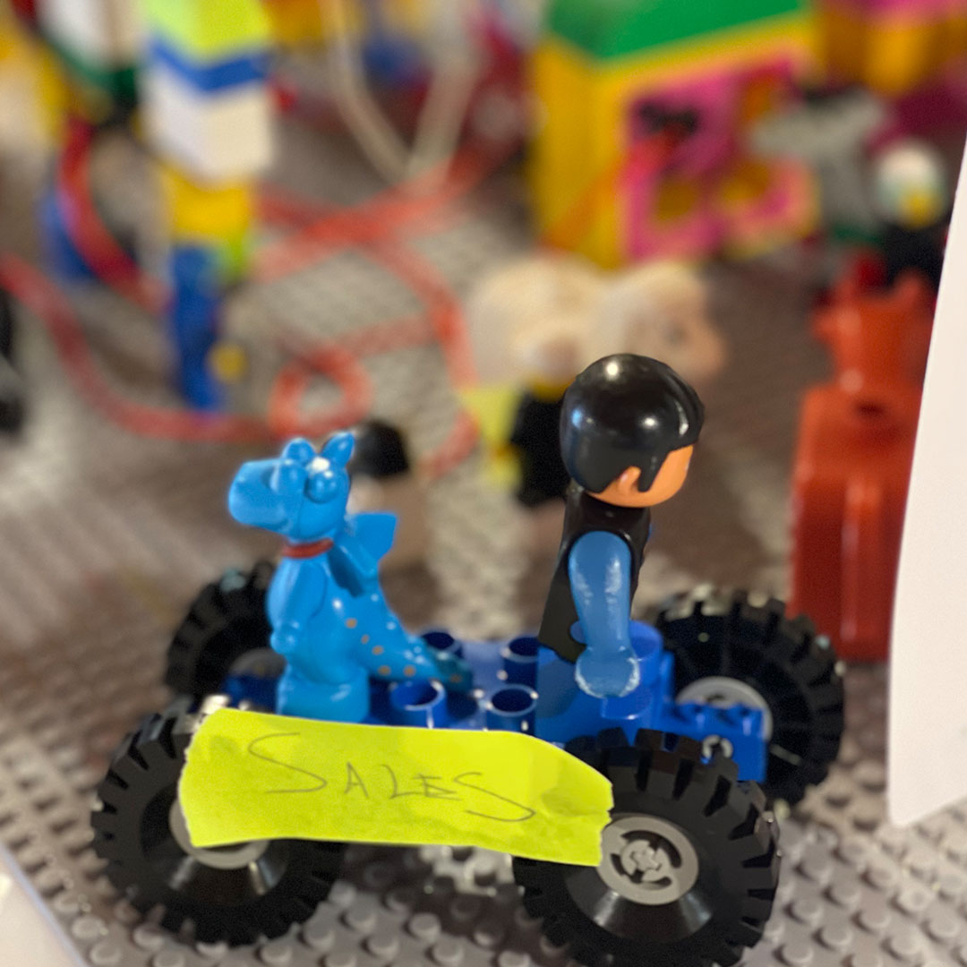 A blue toy vehicle with a dragon and a figure labeled SALES showcases a playful setting amidst colorful building blocks.