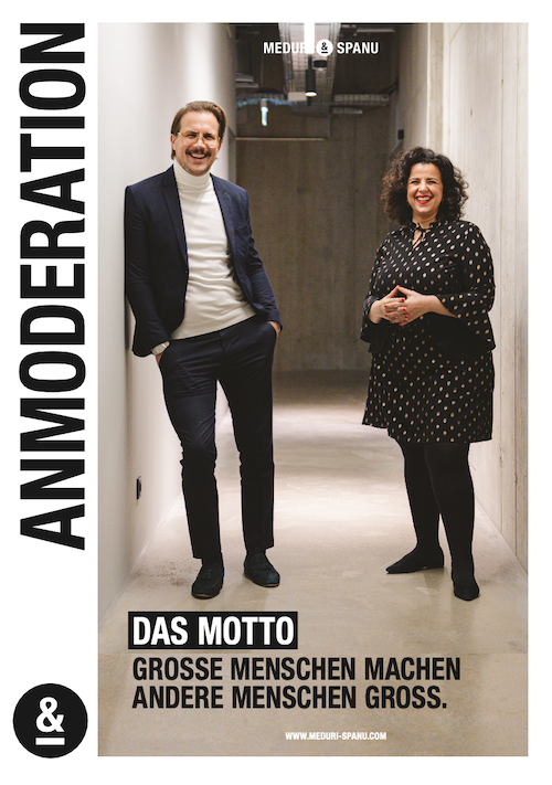 Zwei Moderatoren stehen in einem Korridor, präsentiert mit dem Motto über große Menschen und Inspiration.