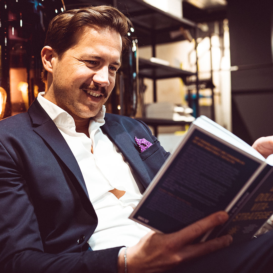 Ein Mann im Anzug liest entspannt ein Buch und genießt das Ambiente in einem modernen Raum mit gedecktem Licht.