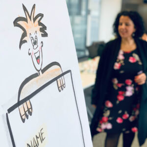 A cartoon character on a flip chart smiles while a woman in a floral dress engages in a meeting.