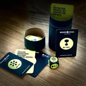 A set of inspirational cards and a die promoting personal growth and collaboration, displayed in a cylindrical container.
