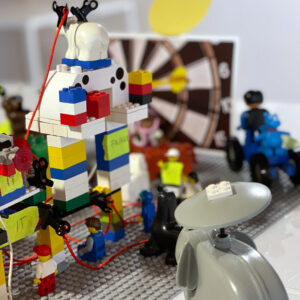Bunte Lego-Modelle mit Figuren, einem Dartboard im Hintergrund und einem stilisierten Elefanten im Vordergrund.